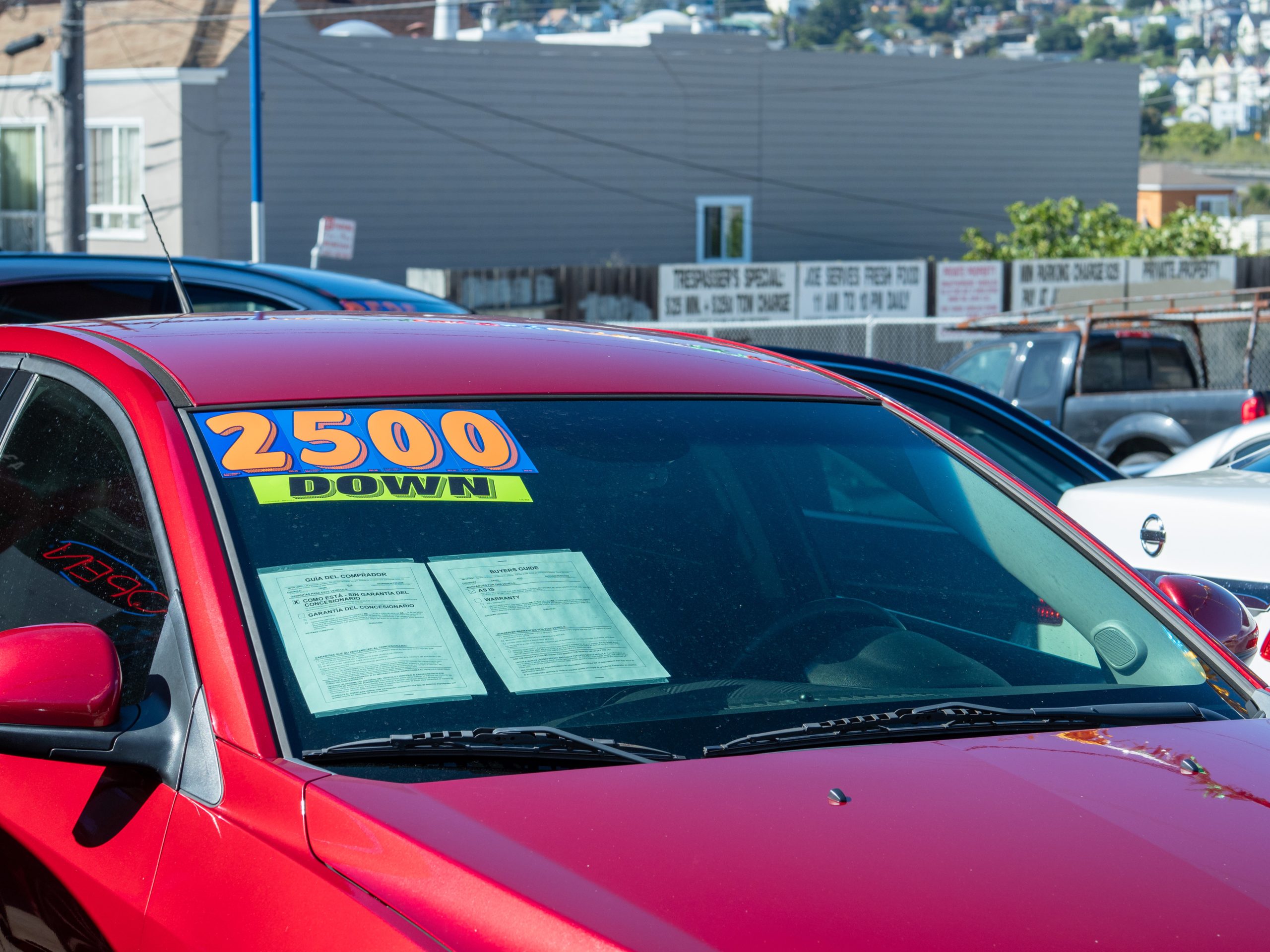 A red car at a used car dealership with a large sticker on the windshield that reads $2500 DOWN in bold orange and yellow letters.